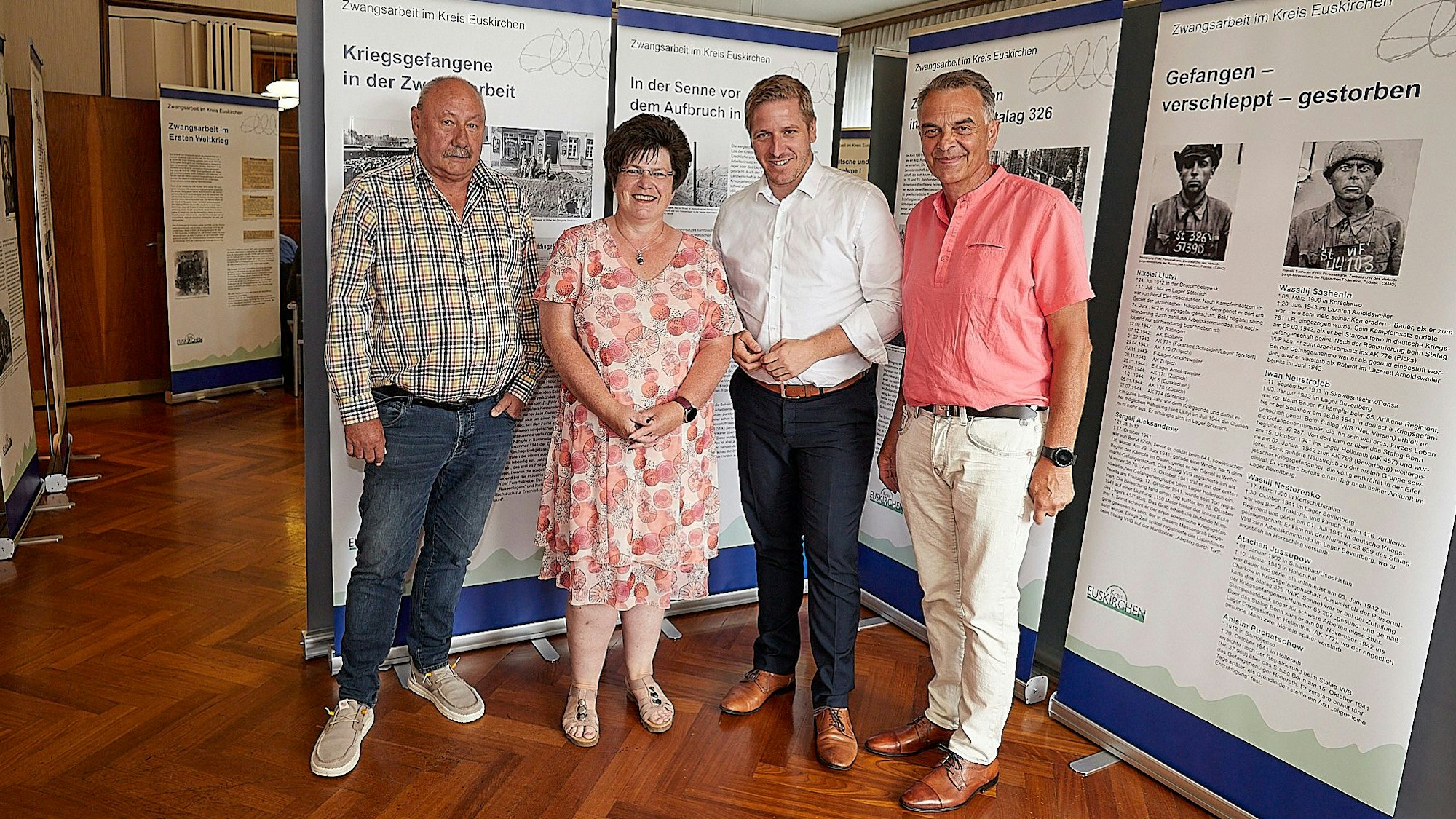 Drei Männer und eine Frau stehen vor den Stellwänden einer Ausstellung.