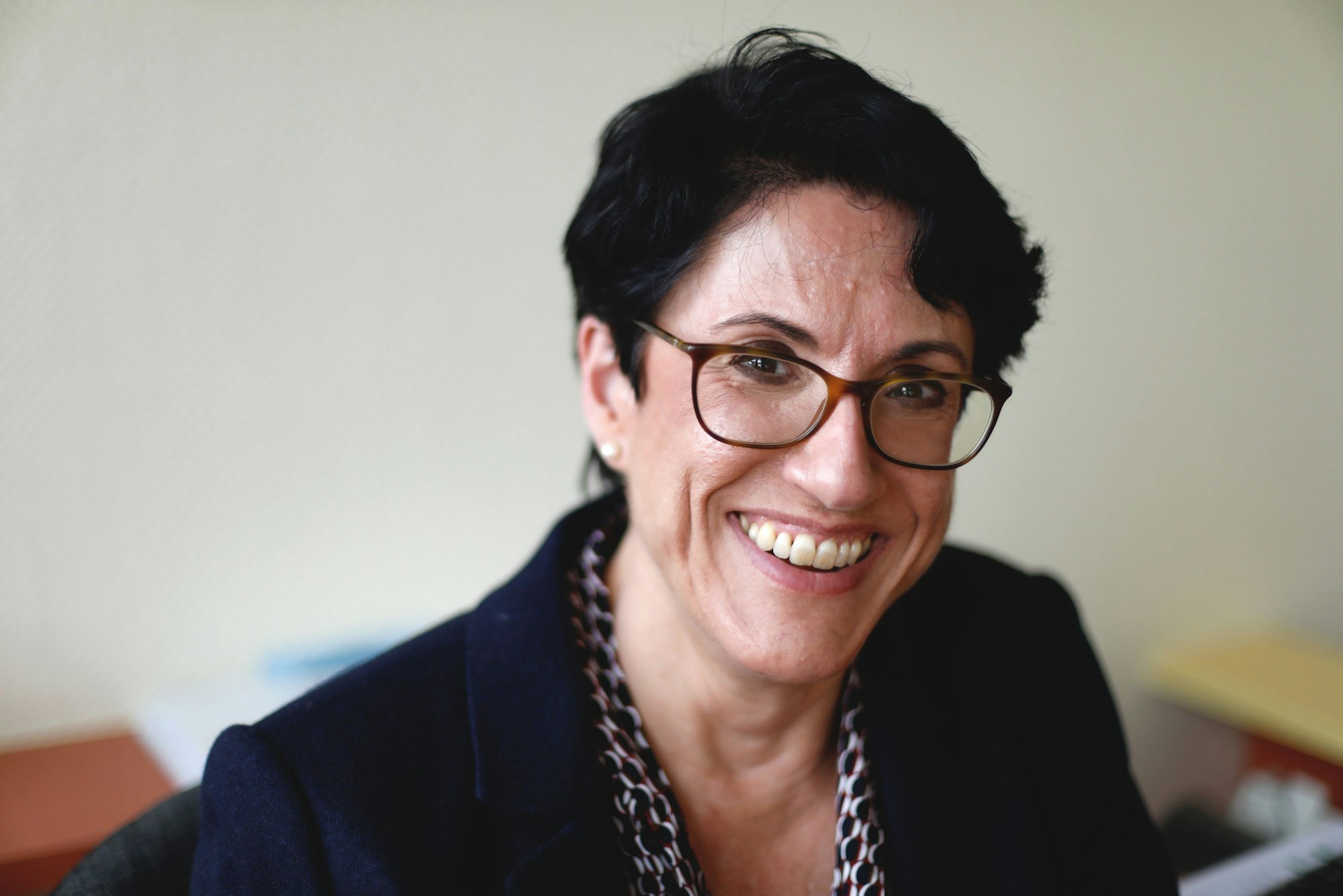 Eine Frau mit kurzen dunklen Haaren und Brille schaut lachend in die Kamera.