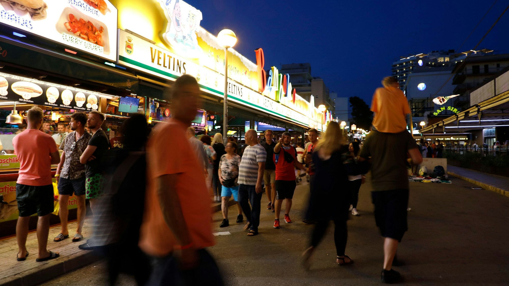 ARCHIV - 14.05.2022, Spanien, Palma: Menschen gehen an der Bar Bamboleo in der Bierstraße am Ballermann vorbei. Im Kampf gegen den sogenannten Sauftourismus auf Mallorca wollen die Hoteliers an der Playa de Palma in diesem Sommer wieder einen Privatdetektiv einsetzen. Foto: Clara Margais/dpa +++ dpa-Bildfunk +++