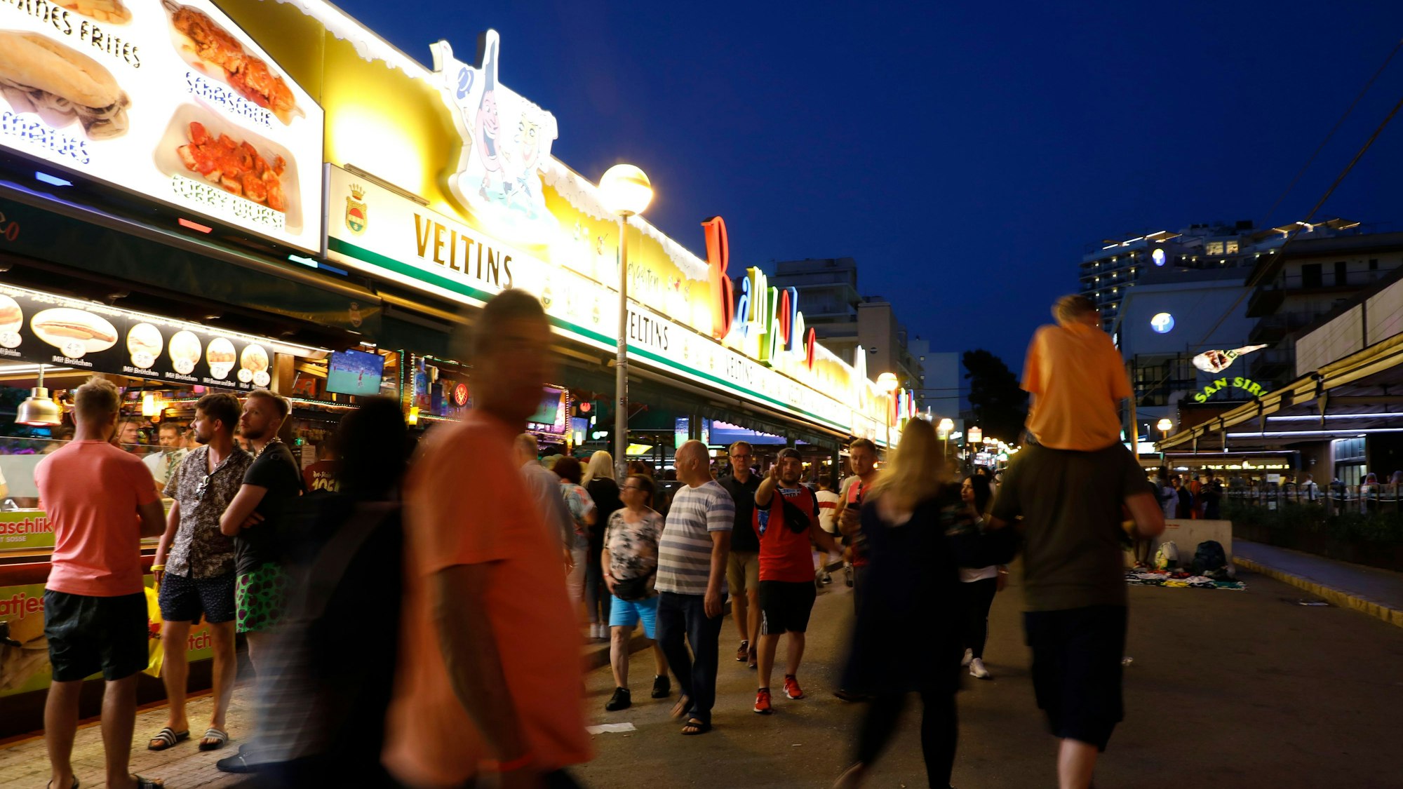 ARCHIV - 14.05.2022, Spanien, Palma: Menschen gehen an der Bar Bamboleo in der Bierstraße am Ballermann vorbei. Im Kampf gegen den sogenannten Sauftourismus auf Mallorca wollen die Hoteliers an der Playa de Palma in diesem Sommer wieder einen Privatdetektiv einsetzen. Foto: Clara Margais/dpa +++ dpa-Bildfunk +++