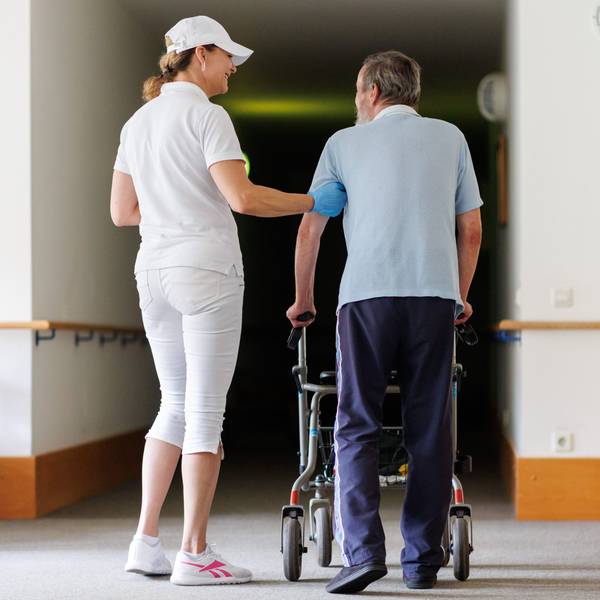 Svetlana (l.), ambulante Pflegefachkraft, begleitet einen Bewohner des Betreuten Wohnens mit seiner Gehhilfe durch das Gebäude. (Symbolbild)