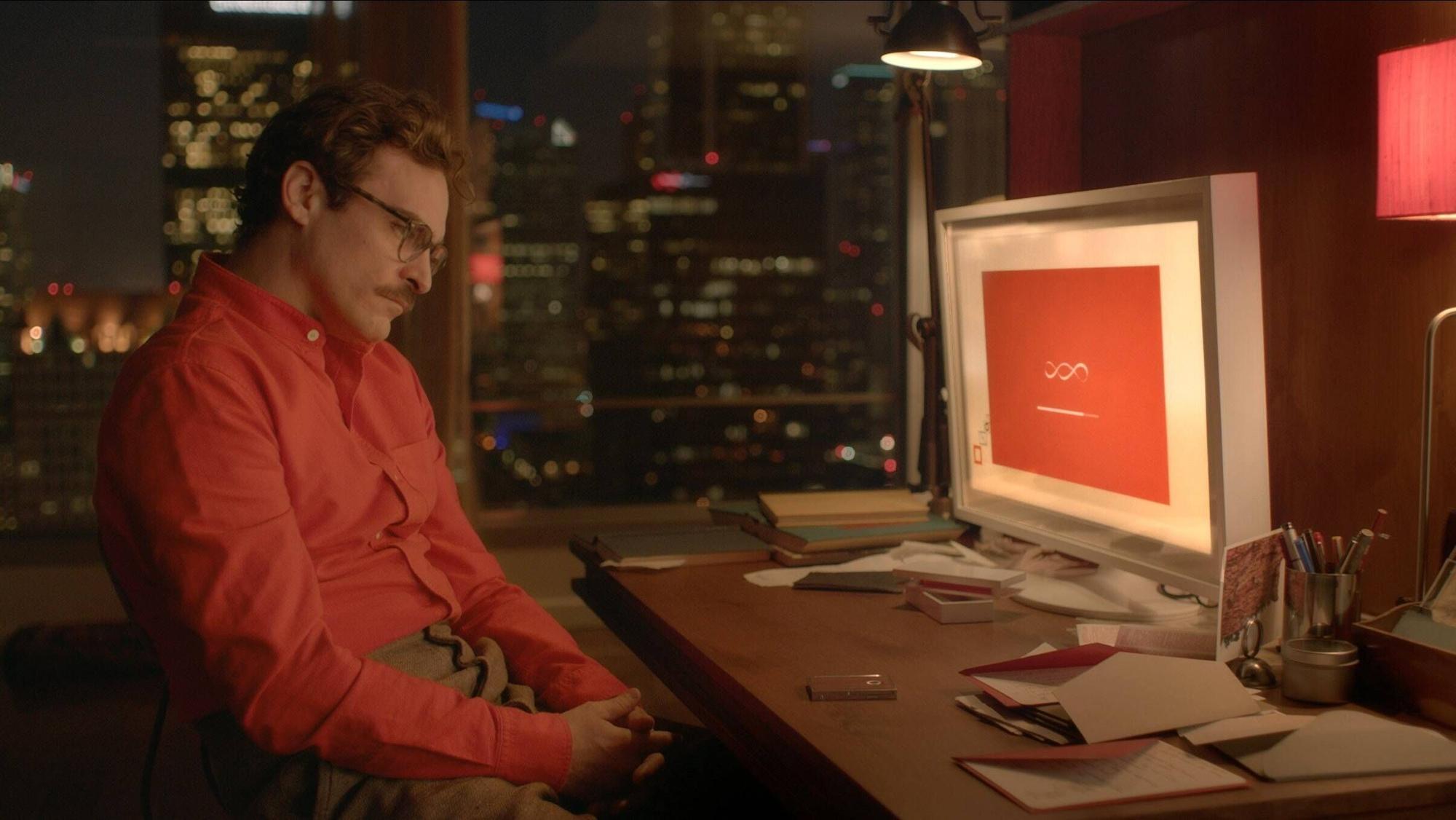 Joaquin Phoenix sitzt im Film „Her“ vor einem Computerbildschirm. Sein oranges Hemd korrespondiert mit dem orangen Hintergrundbild des Betriebssystems.