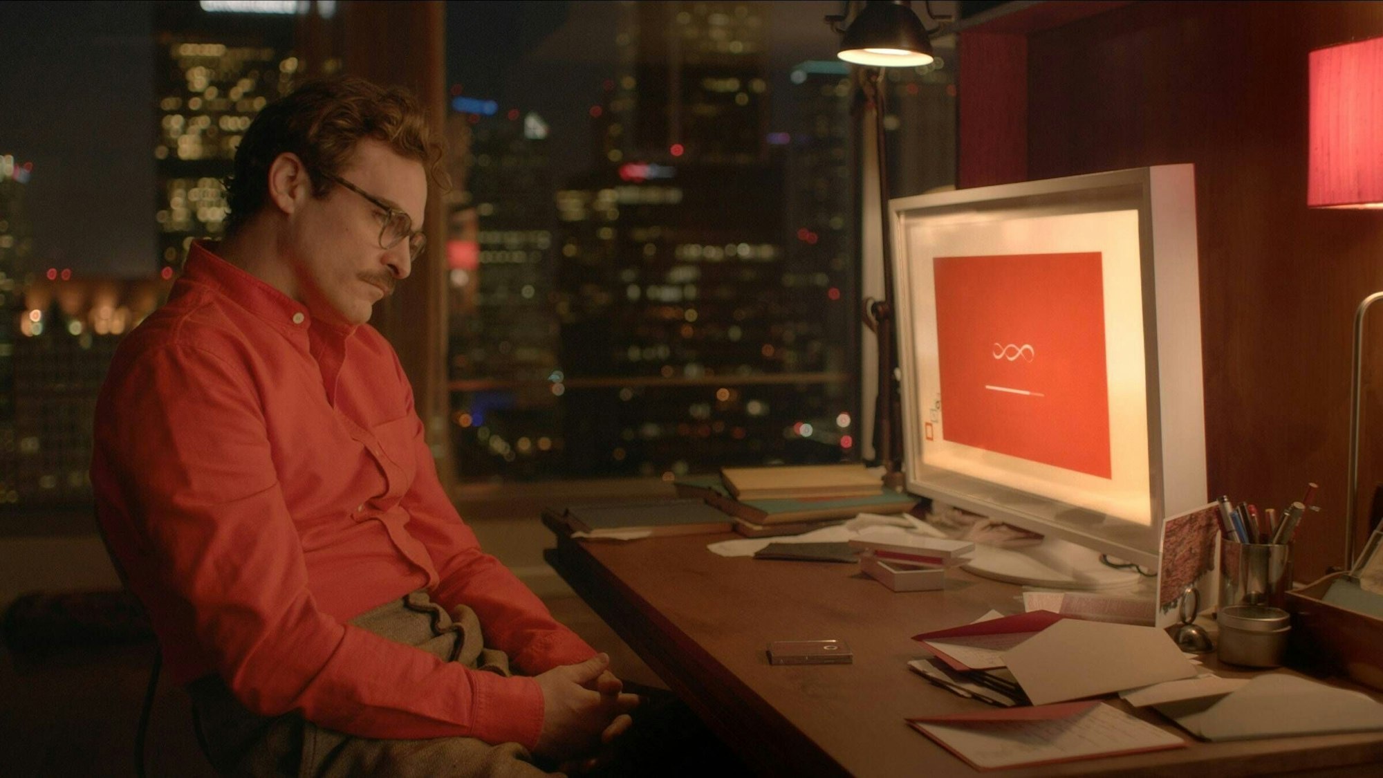 Joaquin Phoenix sitzt im Film „Her“ vor einem Computerbildschirm. Sein oranges Hemd korrespondiert mit dem orangen Hintergrundbild des Betriebssystems.