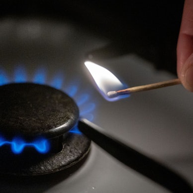 Eine Gasflamme wird auf einem Küchenherd mit einem Streichholz entzündet.