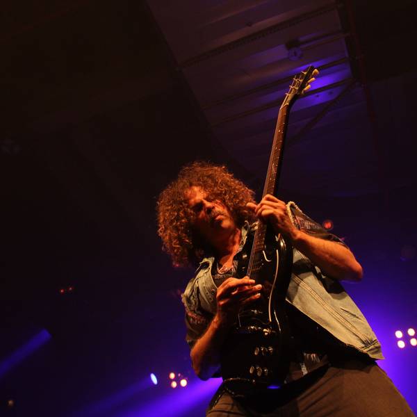 Andrew Stockdale von Wolfmother ist in sein Gitarrenspiel vertieft. Im Hintergrund glimmen die Bühnenscheinwerfer.
