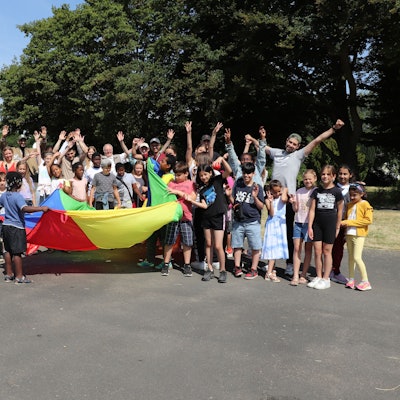 Viele Kinder in Jubelpose sind zu sehen. Einige halten ein buntes Tuch.