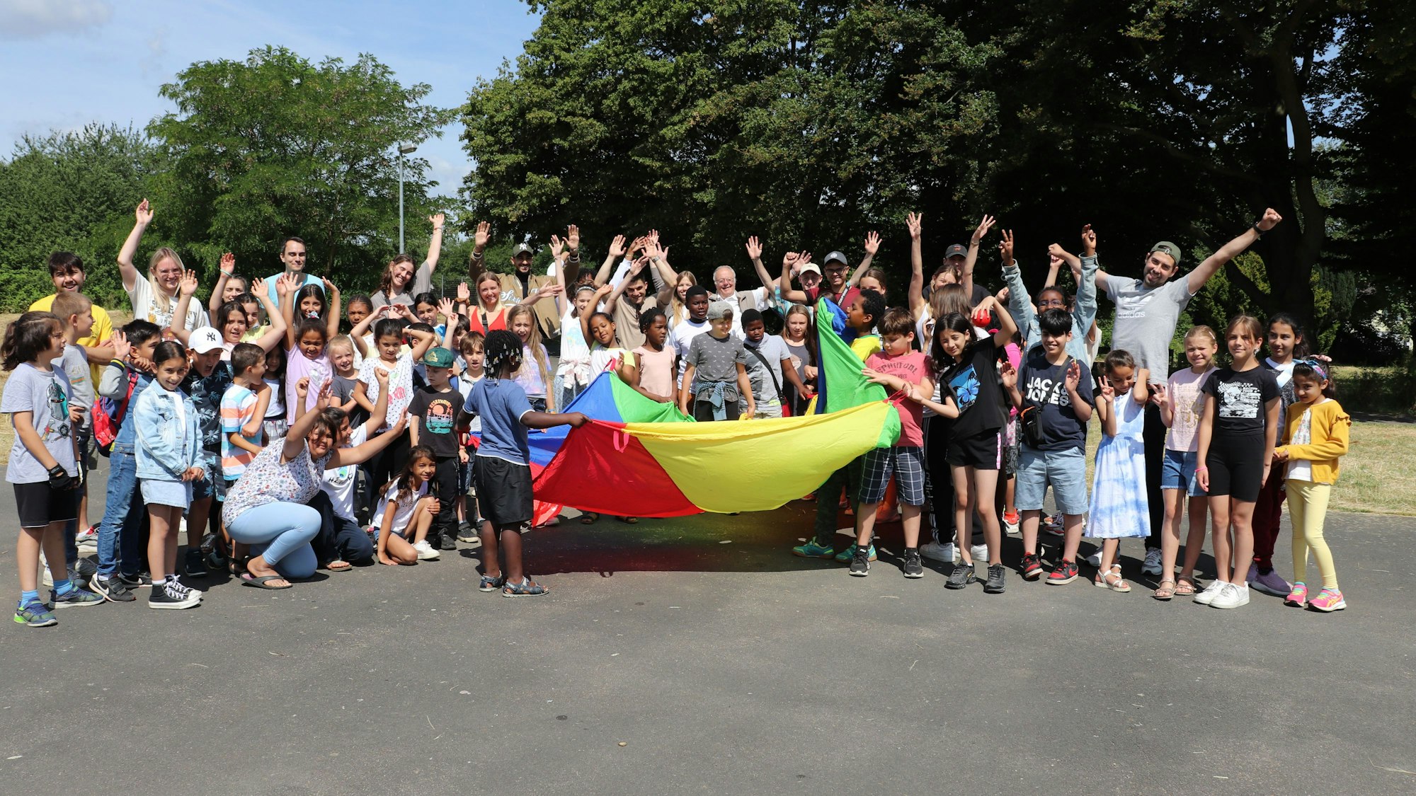 Viele Kinder in Jubelpose sind zu sehen. Einige halten ein buntes Tuch.