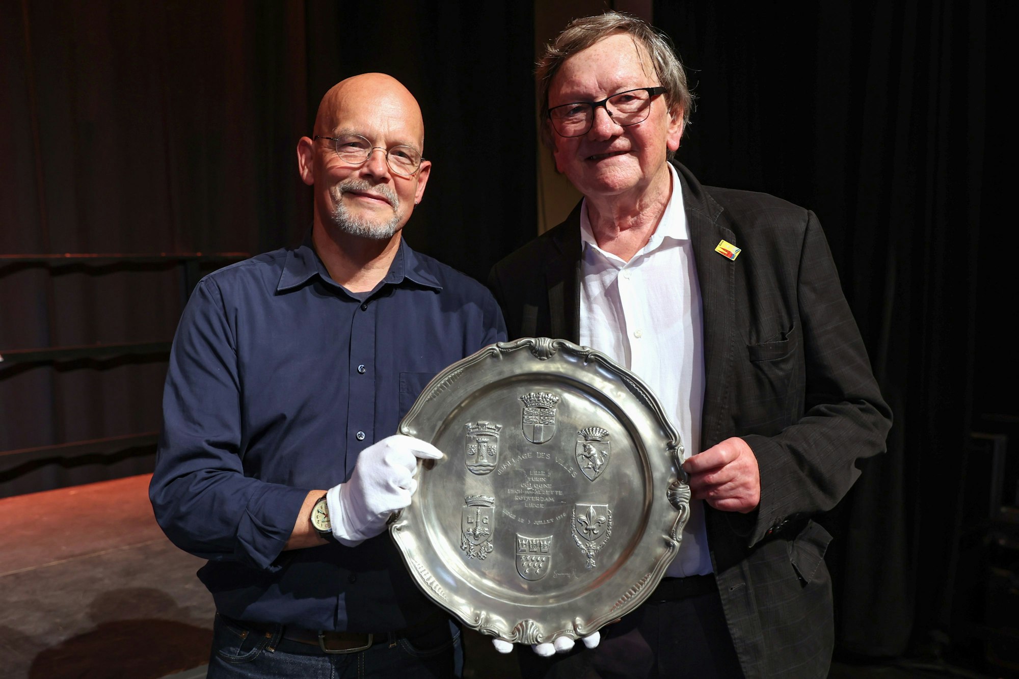 Volker Thiel von dem Haus der Geschichte und Hemann Jakob vom Freundeskreis Köln-Turin Foto halten den Zinnteller, der an den Gründungstag der Ringpartnerschaft erinnert, in den Händen.
