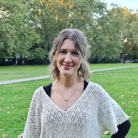 Eine junge Frau mit blondem kinnlangem Haar steht in einem Park.