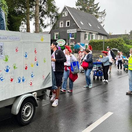 Ein Wagen mit QR-Code rollt durch den Ort, dahin Feiernde.