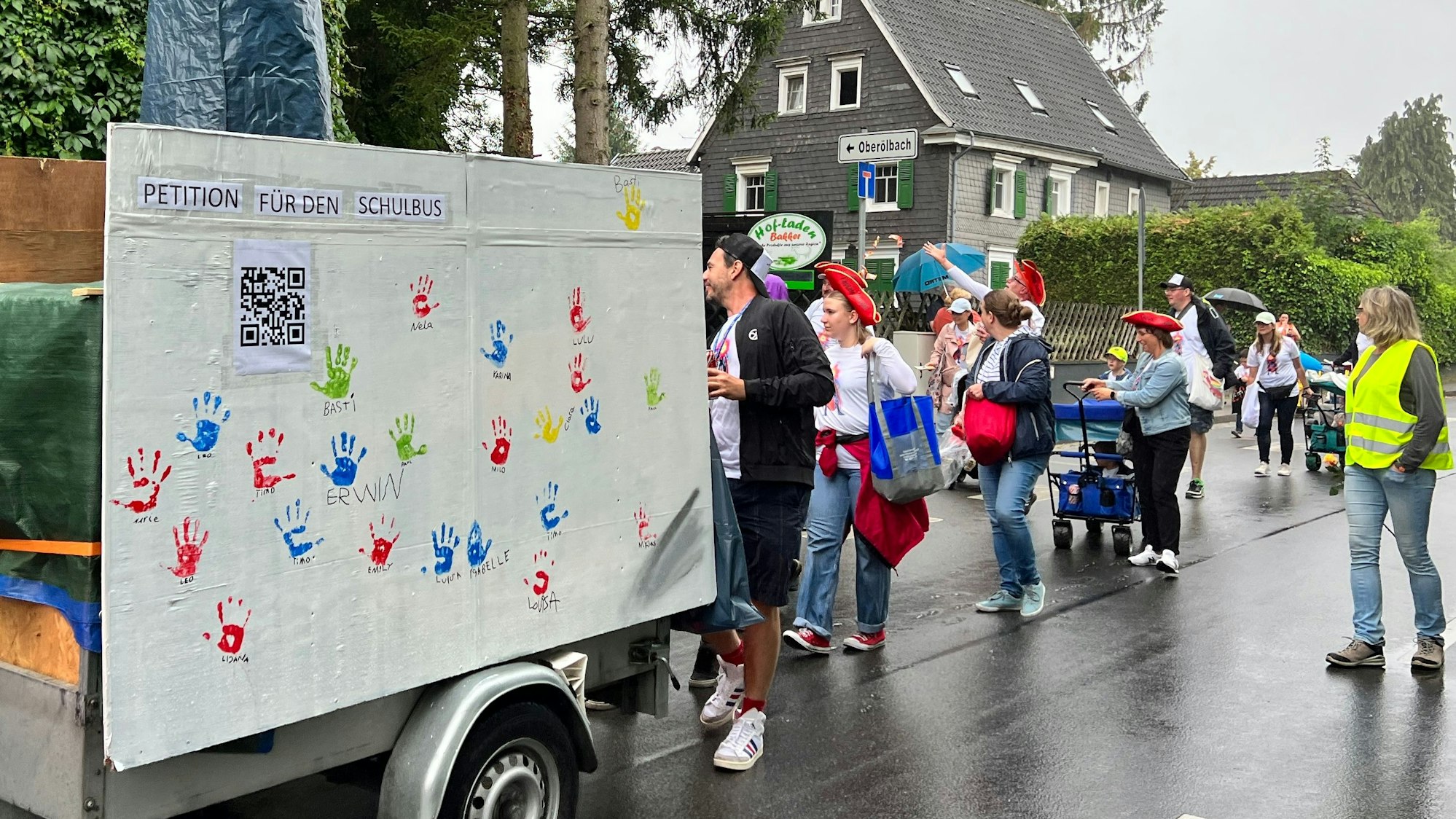 Ein Wagen mit QR-Code rollt durch den Ort, dahin Feiernde.