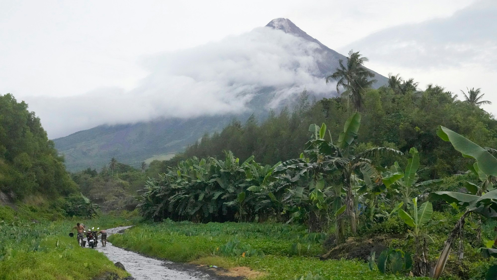 09.06.2023, Philippinen, Bonga: Männer waschen ihre Motorräder an einem Fluss in der Nähe des Vulkans Mayon in Bonga in der Provinz Albay im Nordosten der Philippinen.