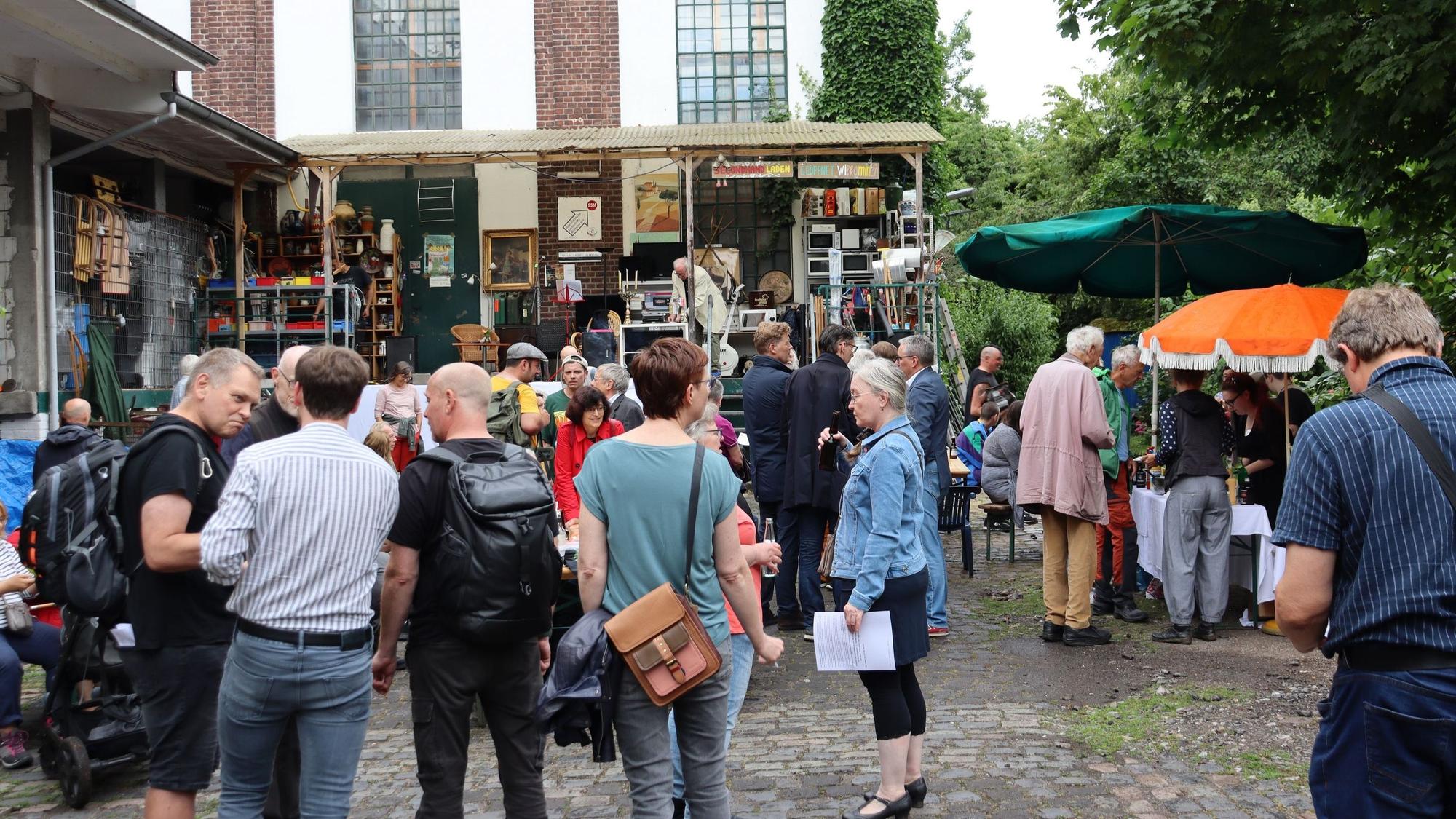 Viele Menschen stehen auf dem Vorplatz eines fabrikartigen Gebäudes.