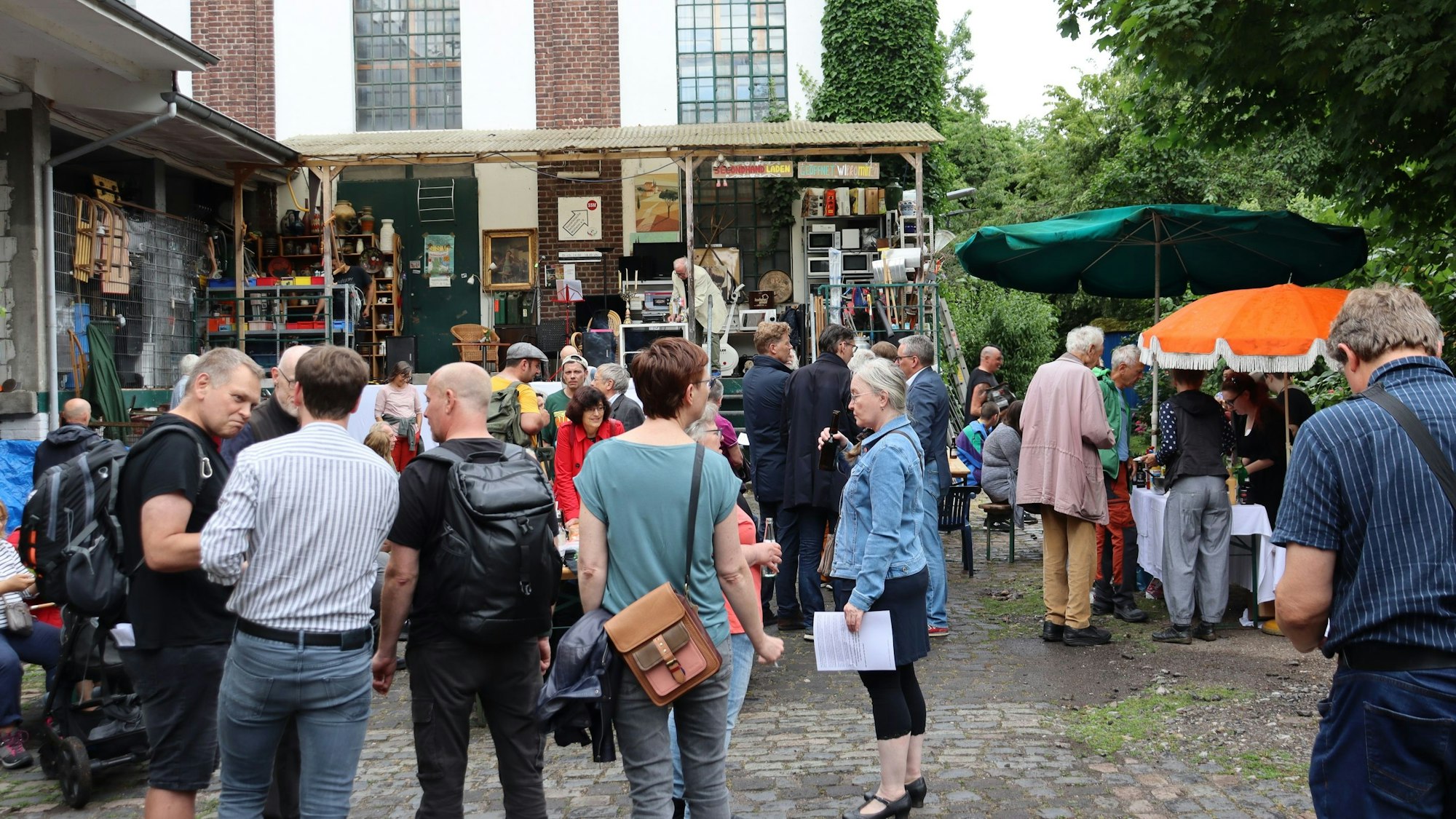 Viele Menschen stehen auf dem Vorplatz eines fabrikartigen Gebäudes.