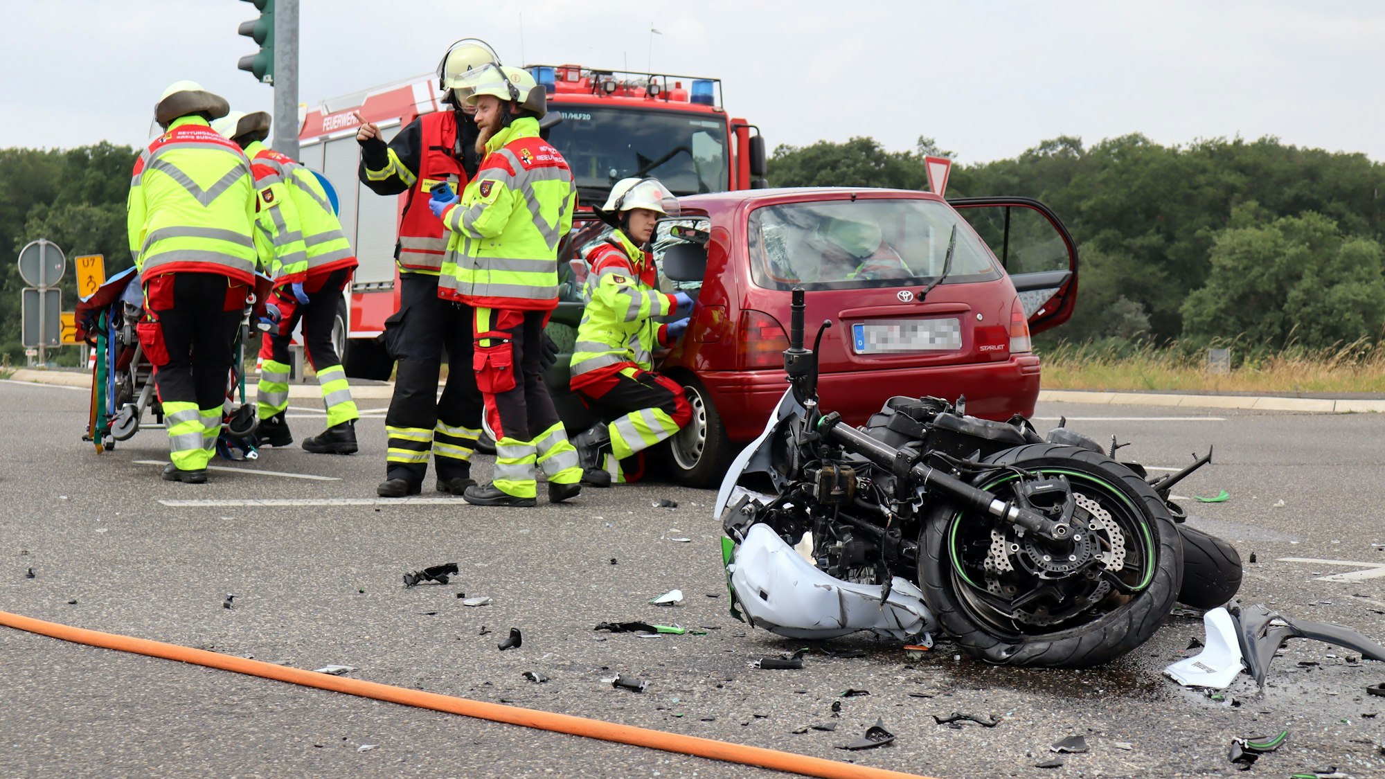 Rettungskräfte kümmern sich um einen Patienten in einem Auto. Im Vordergrund liegt das zerstörte Motorrad.