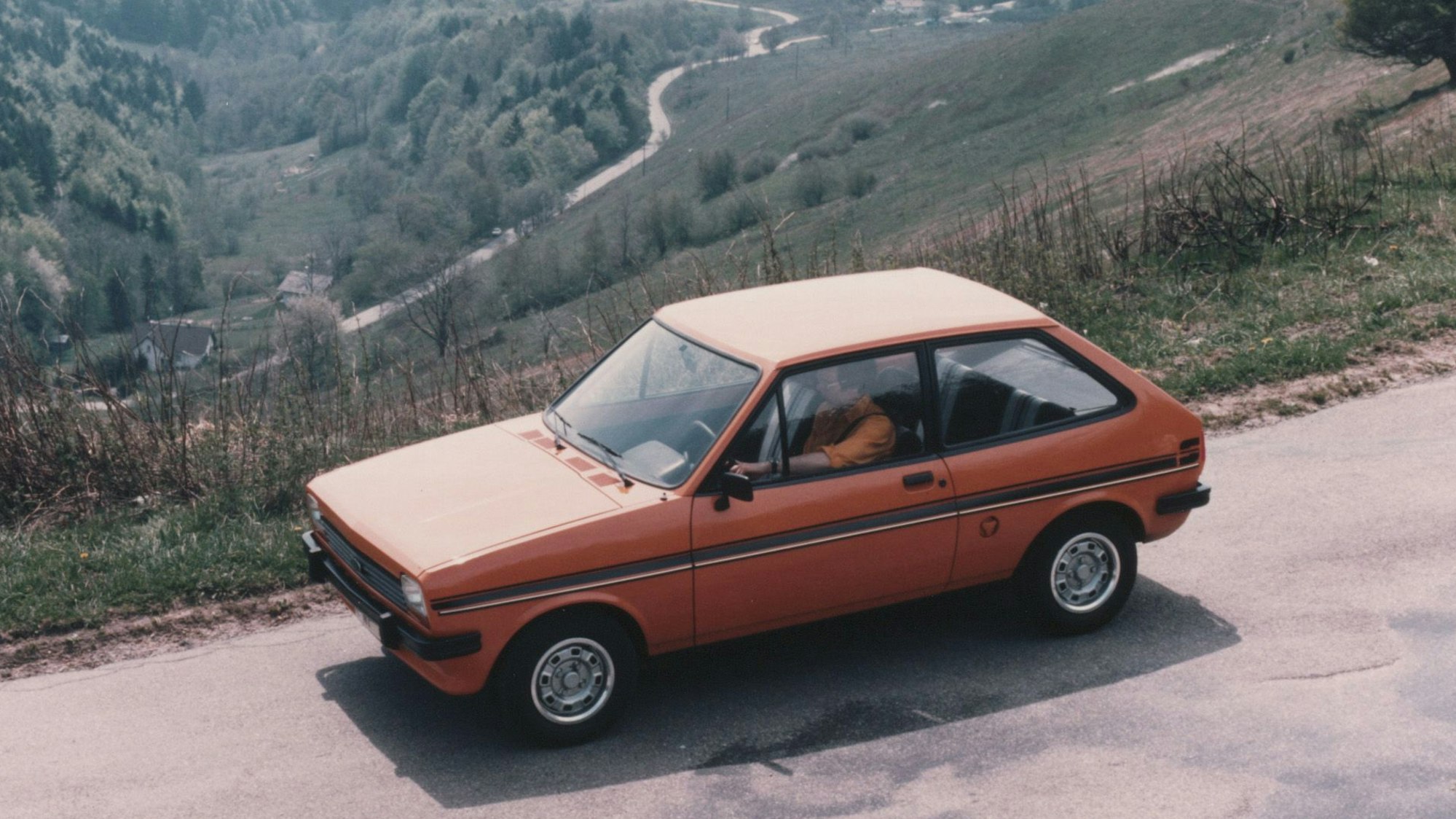 Ford-Werk in Köln: Ein roter Ford Fiesta der ersten Generation fährt auf einer Landstraße.