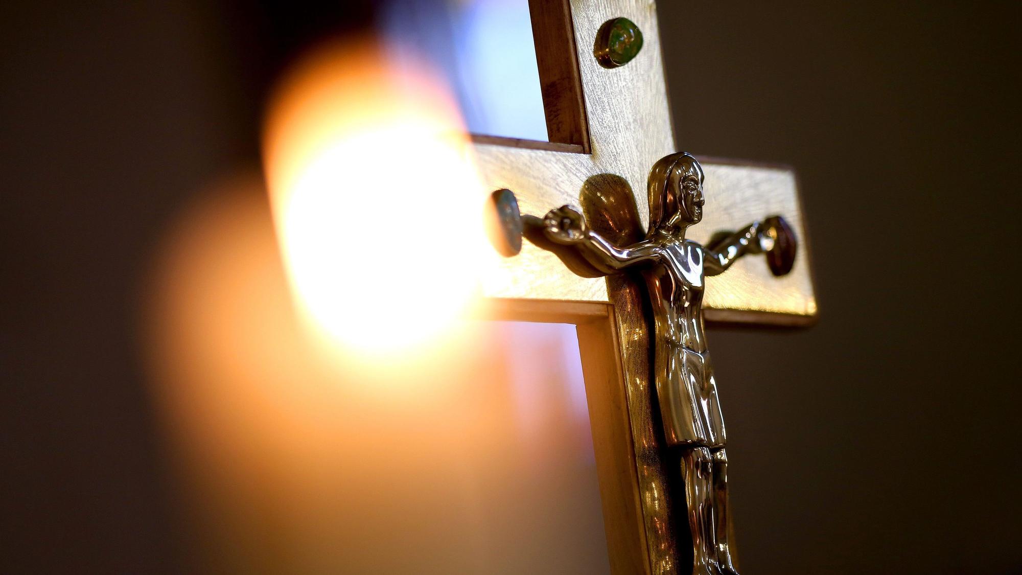 Ein Jesuskreuz und eine brennende Kerze stehen in einer Kirche.