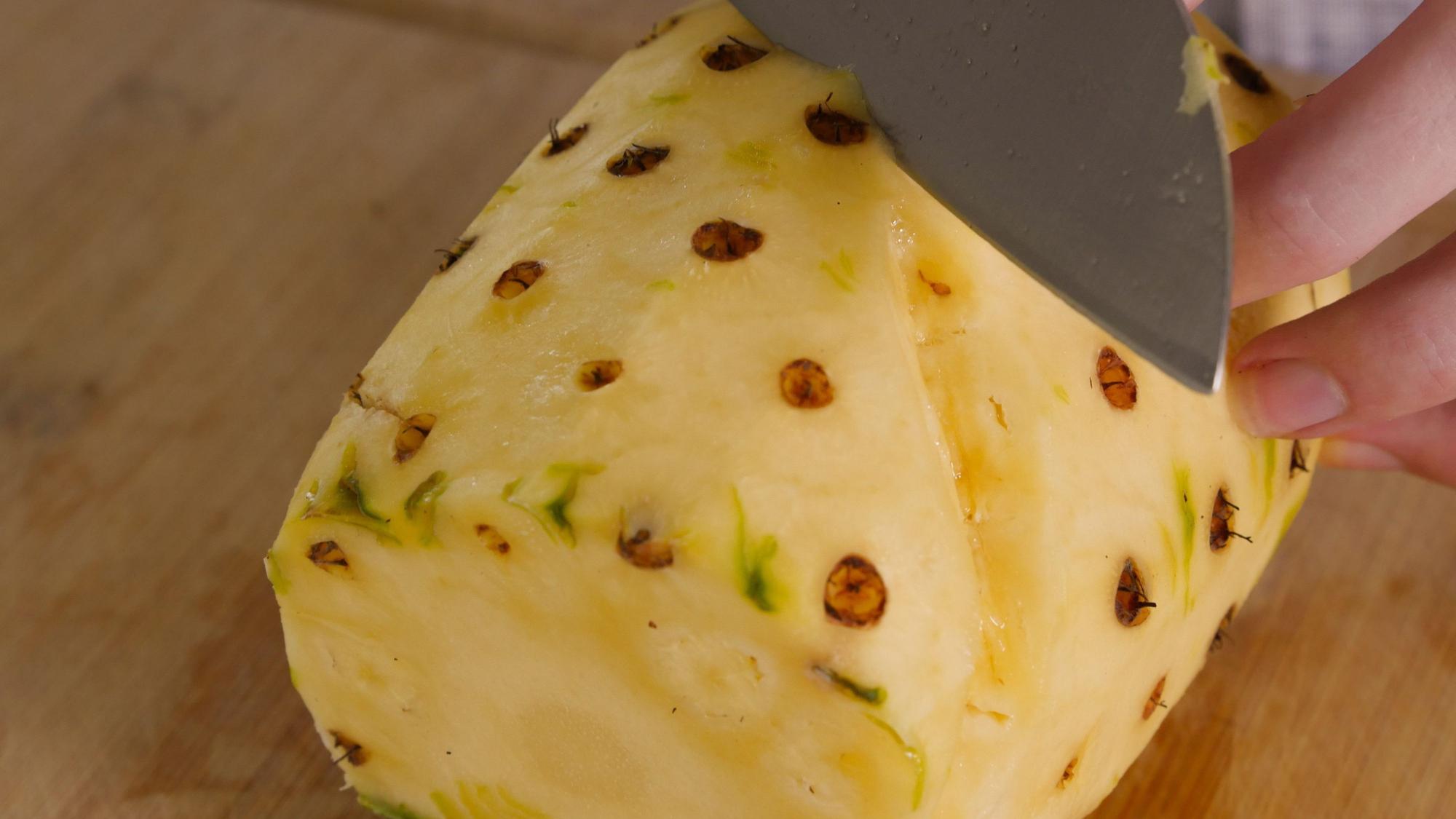 aus einer Ananas werden mit einem Messer braune Punkte herausgeschnitten