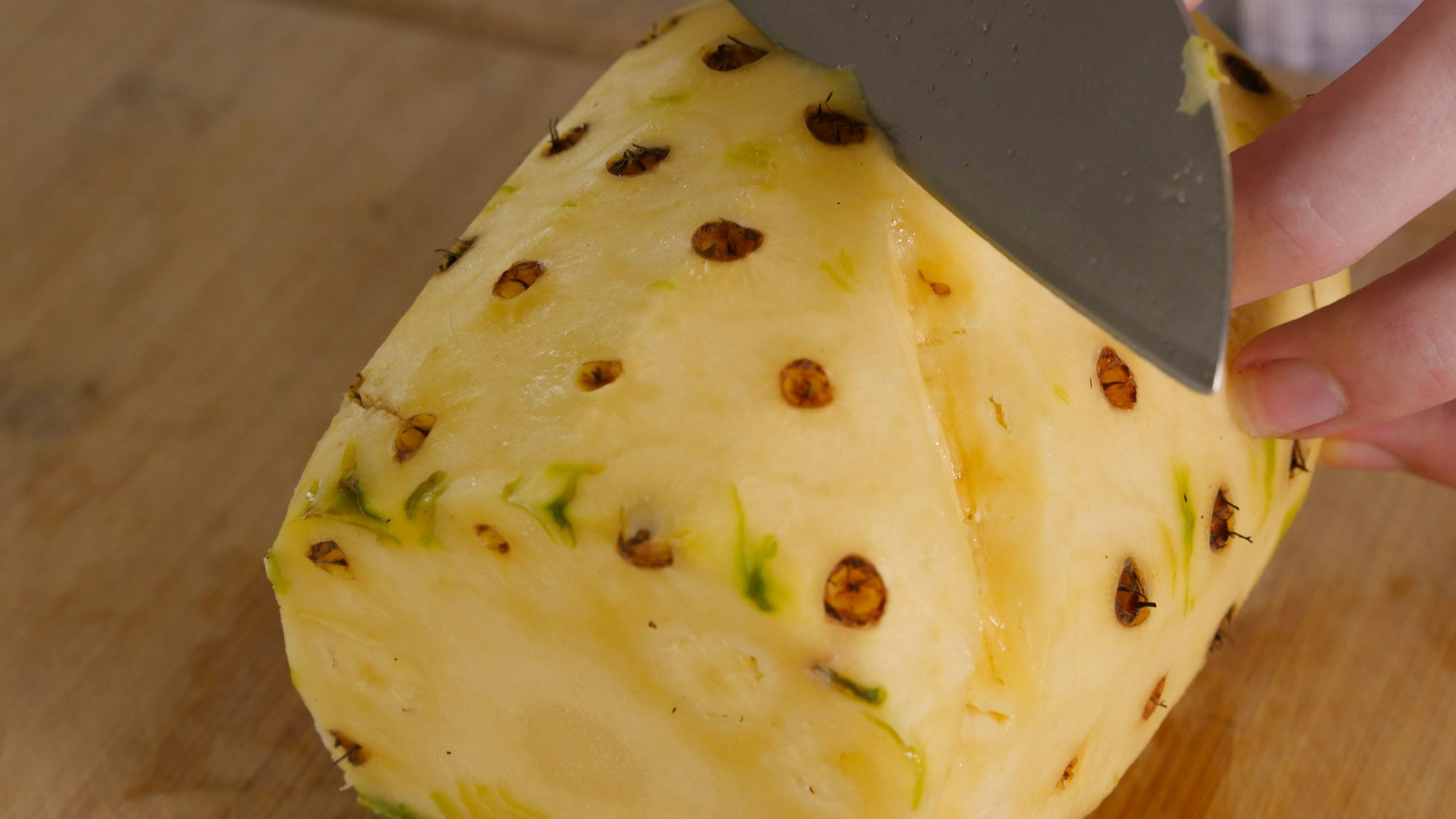 aus einer Ananas werden mit einem Messer braune Punkte herausgeschnitten