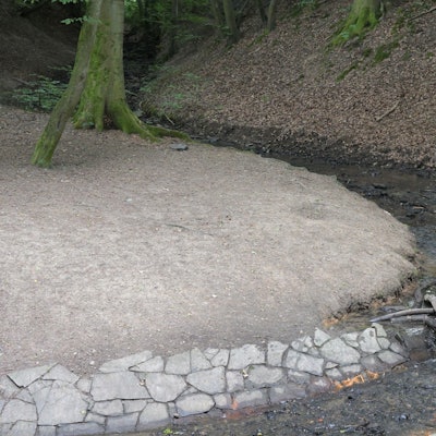 Eine Person entnimmt illegal Wasser aus dem Milchbornbach. In der Hand hält sie einen blauen Kanister.