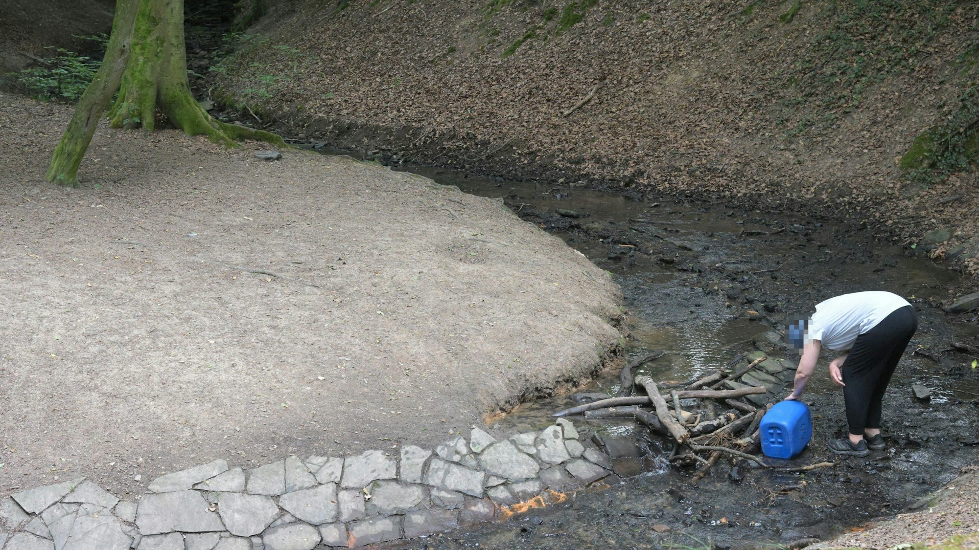 Eine Person entnimmt illegal Wasser aus dem Milchbornbach. In der Hand hält sie einen blauen Kanister.