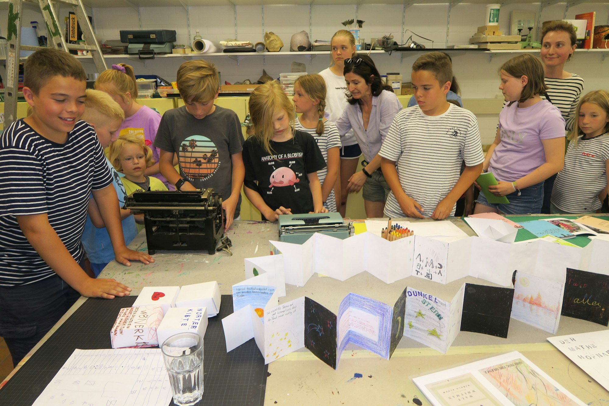 Viele Kinder stehen um einen Tisch. Darauf sind selbstgemachte Bücher zu sehen.