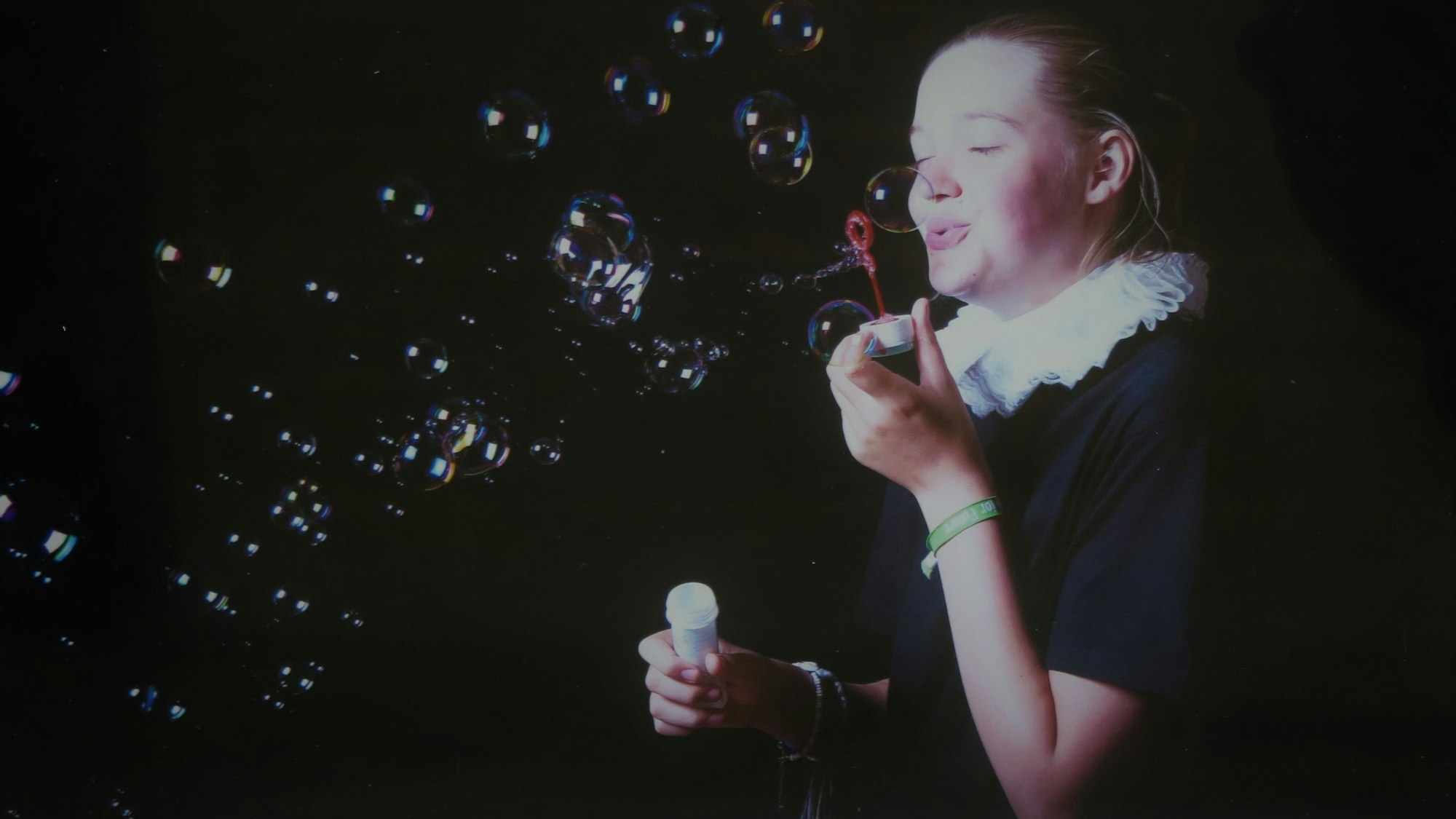 Ein Mädchen mit einer weißen Halskrause pustet Seifenblasen.