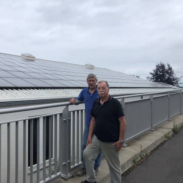 Zwei Männer vor einem Haus, auf dessen Dach Solarmodule sind.