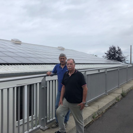 Zwei Männer vor einem Haus, auf dessen Dach Solarmodule sind.