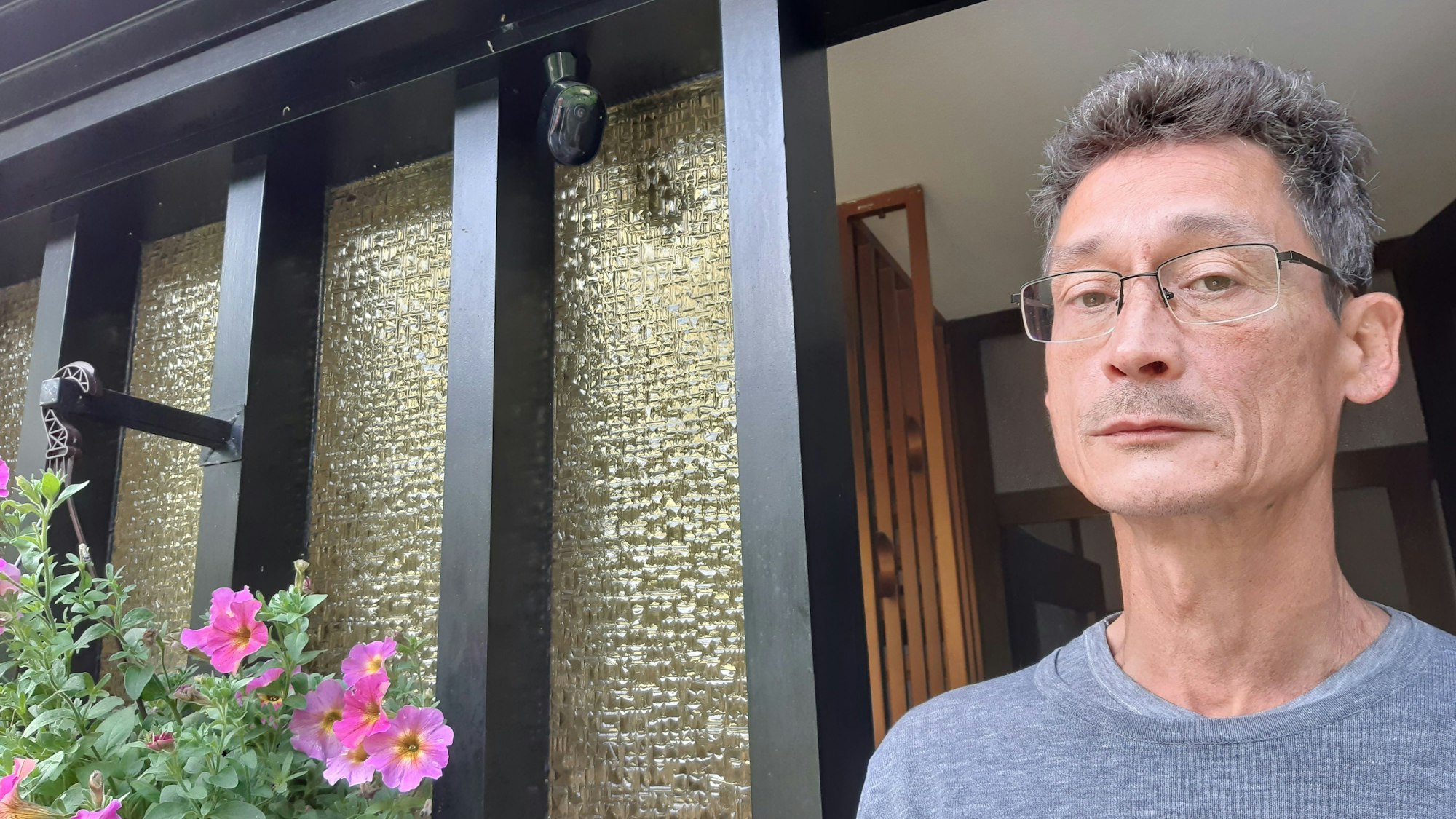 Ein Mann steht neben einer Überwachungskamera an einer Haustür.