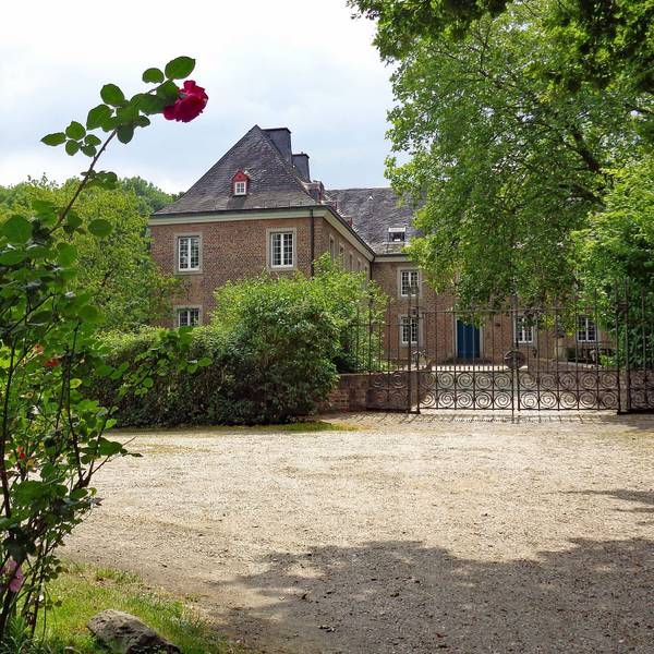 Die Burg Bachem in Frechen, umgeben von Grün und Rosenbüschen.