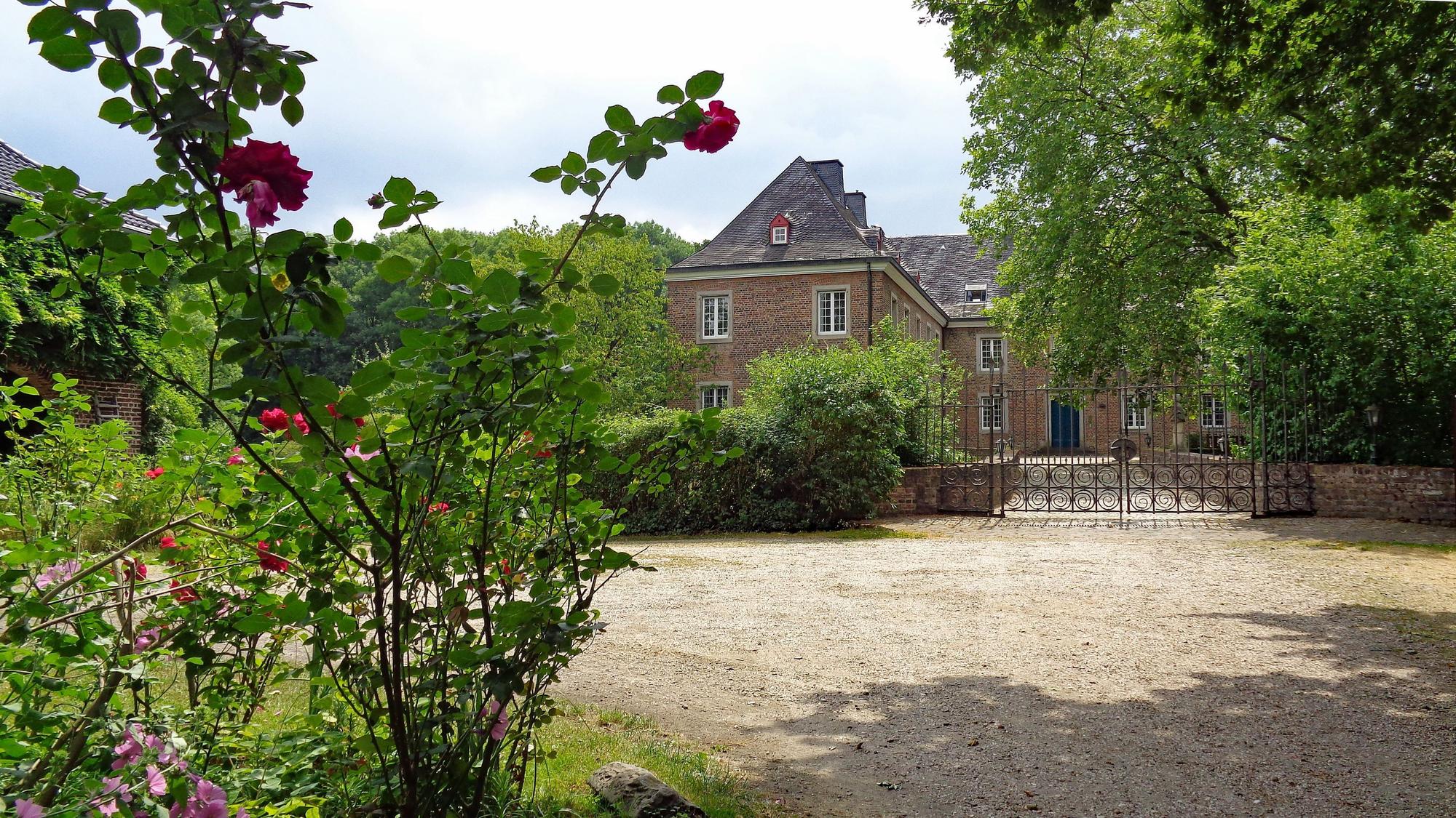 Die Burg Bachem in Frechen, umgeben von Grün und Rosenbüschen.