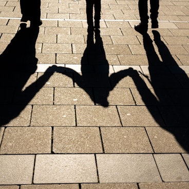 Die Schatten von zwei Erwachsenen und einem Kind fallen in den Morgenstunden auf den Asphalt.