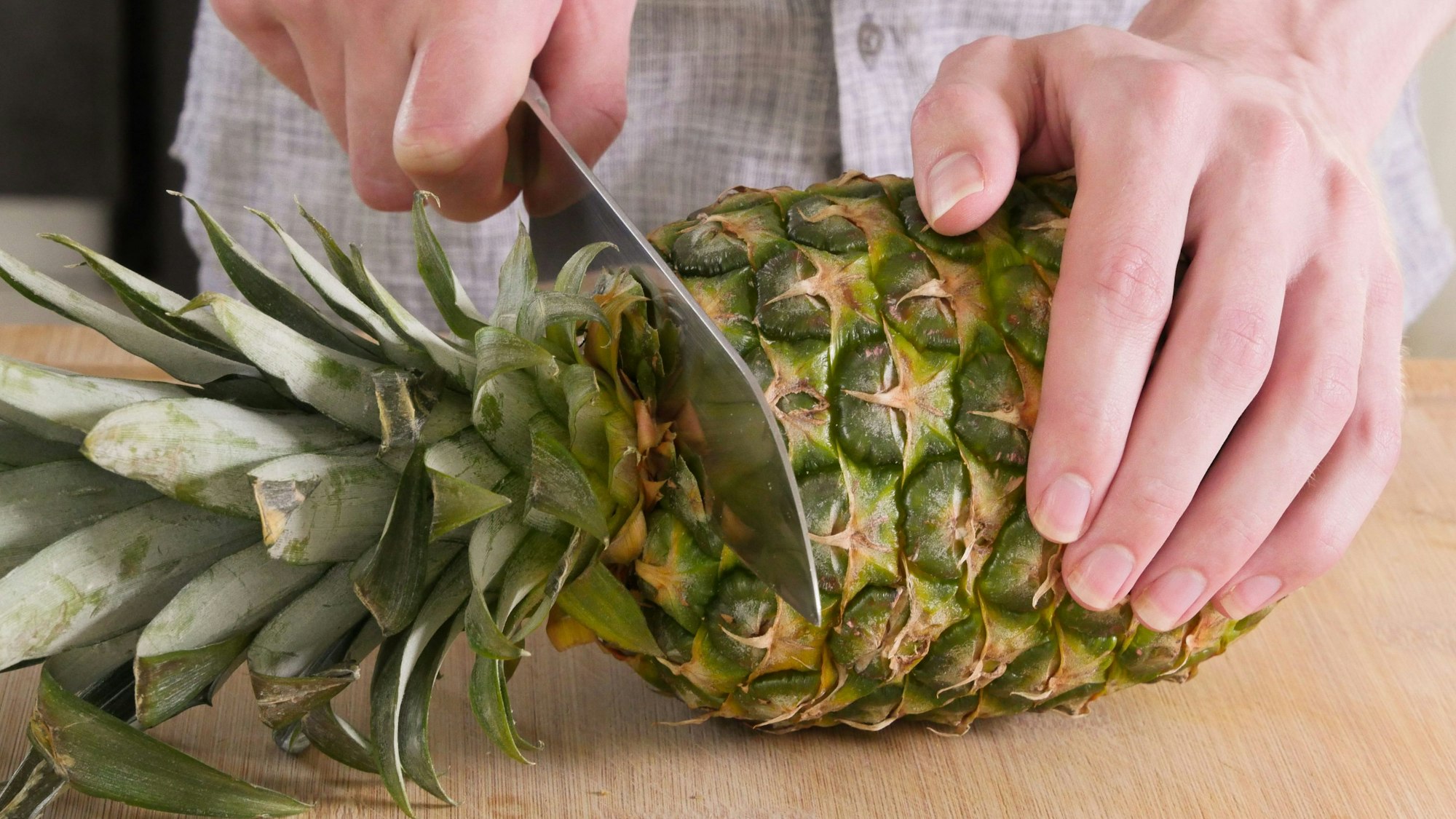ein Mann schneidet den oberen Teil einer Ananas ab