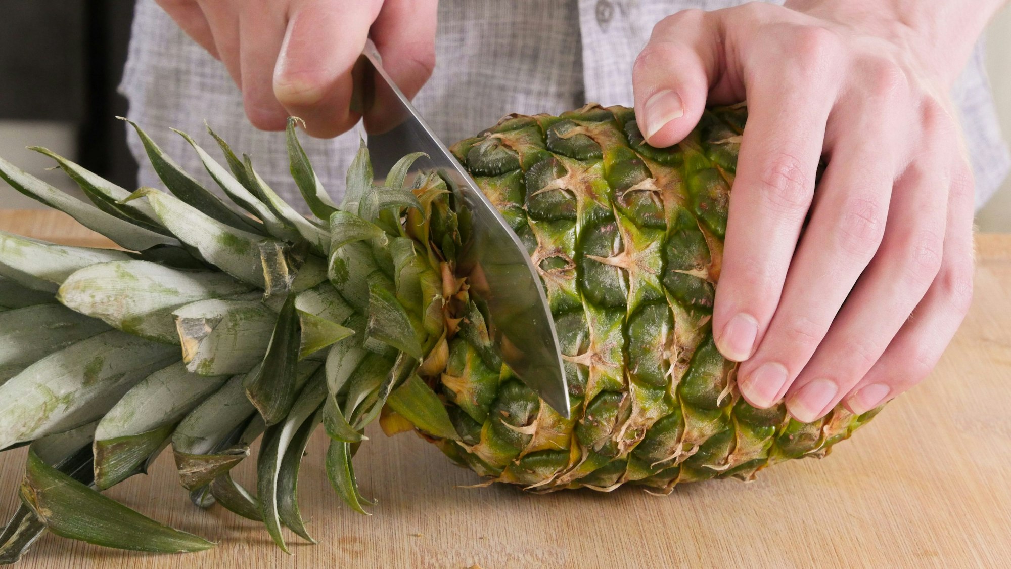 Mann schneidet eine Ananas auf einem Holzbrett