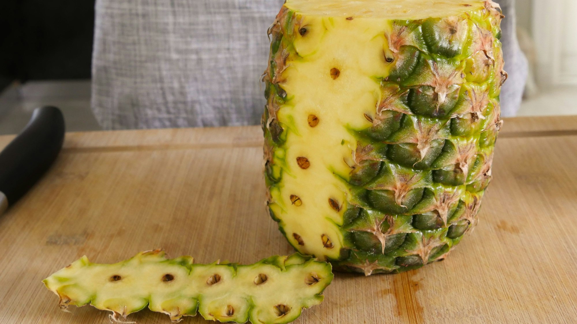 Ananas auf einem Schneidebrett, ein Teil der Schale liegt neben der Frucht