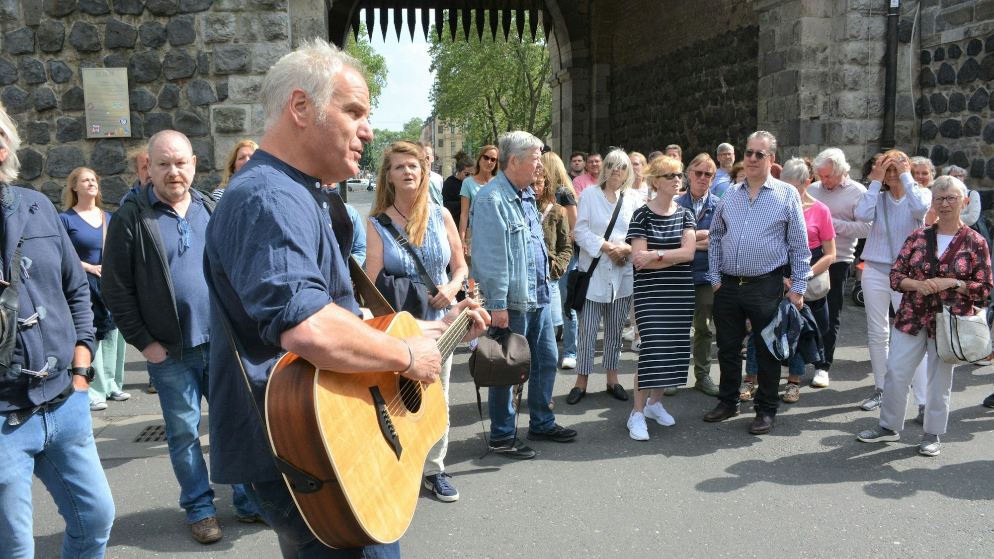 Josef Loup steht mit seiner Gitarre vor einer Gruppe von Leuten an der Severinstorburg.