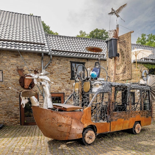 Das Foto zeigt ein aus Schrott und Abfall gebautes Kunstobjekt auf Rädern.