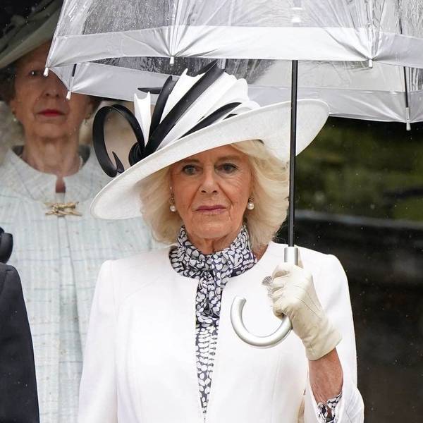 Königin Camilla mit Regenschirm und weißem Outfit.
