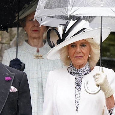 Königin Camilla mit Regenschirm und weißem Outfit.