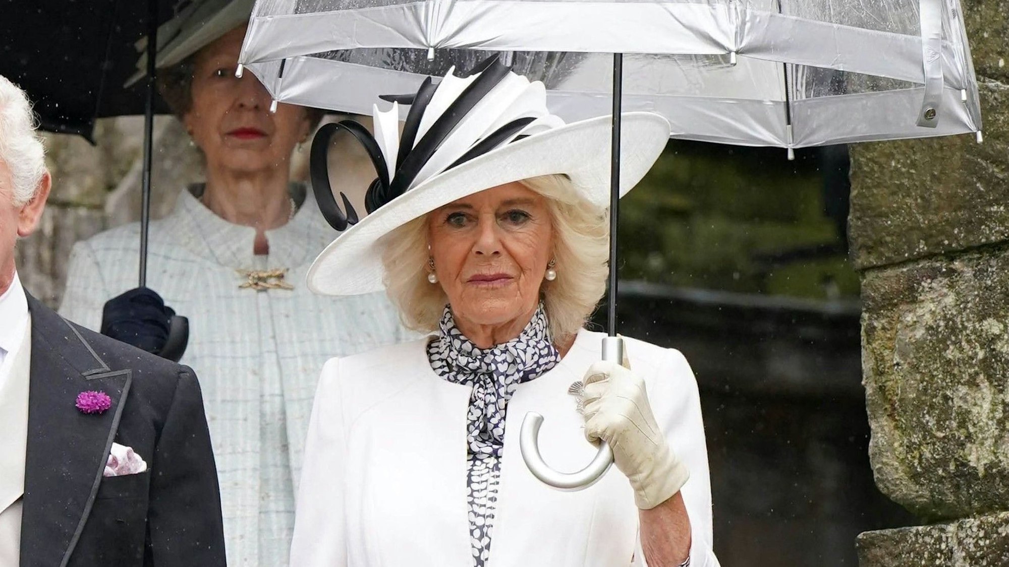 Königin Camilla mit Regenschirm und weißem Outfit.