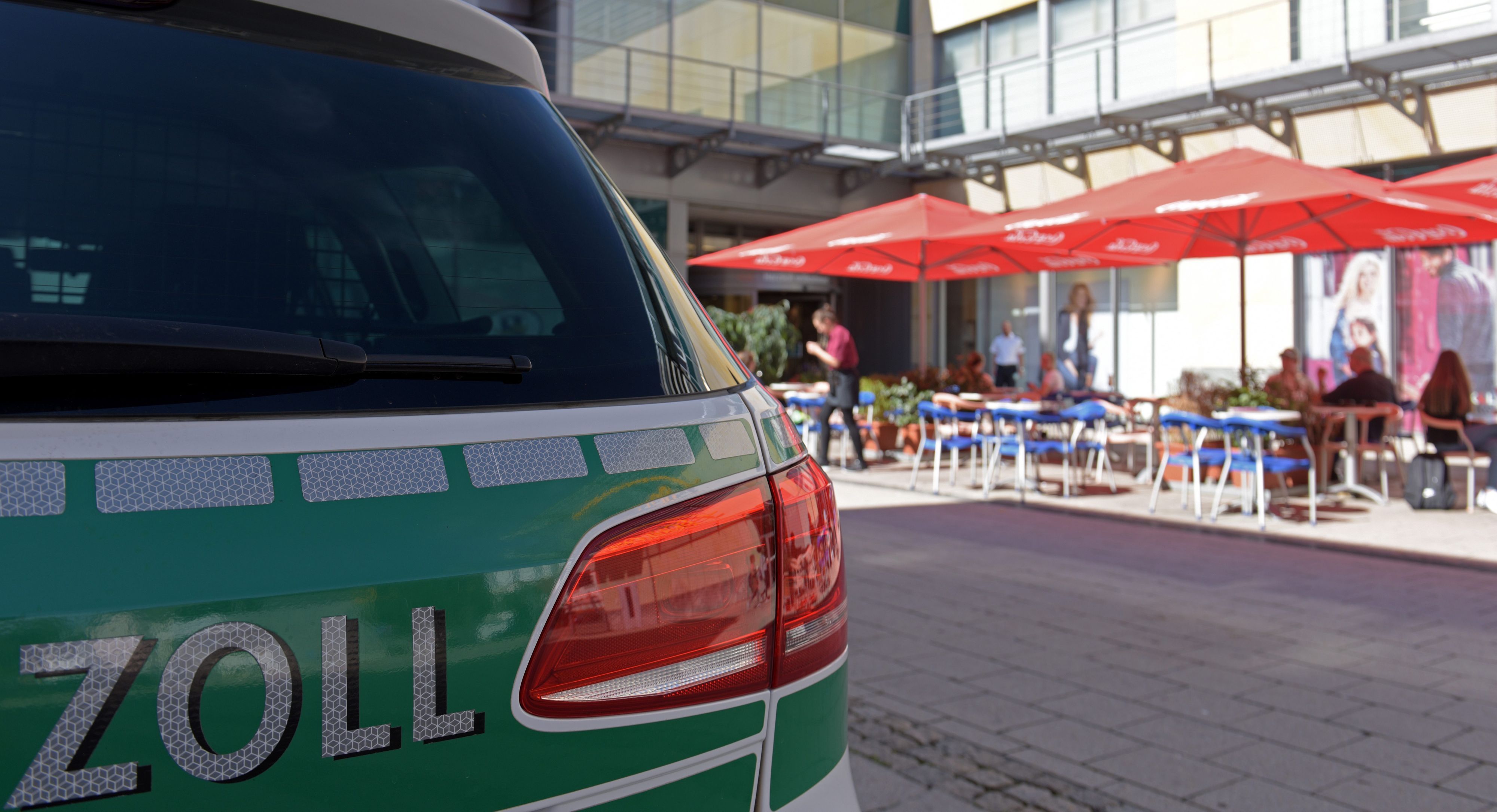 Vor einem Straßencafé steht ein Streifenwagen des Zolls.