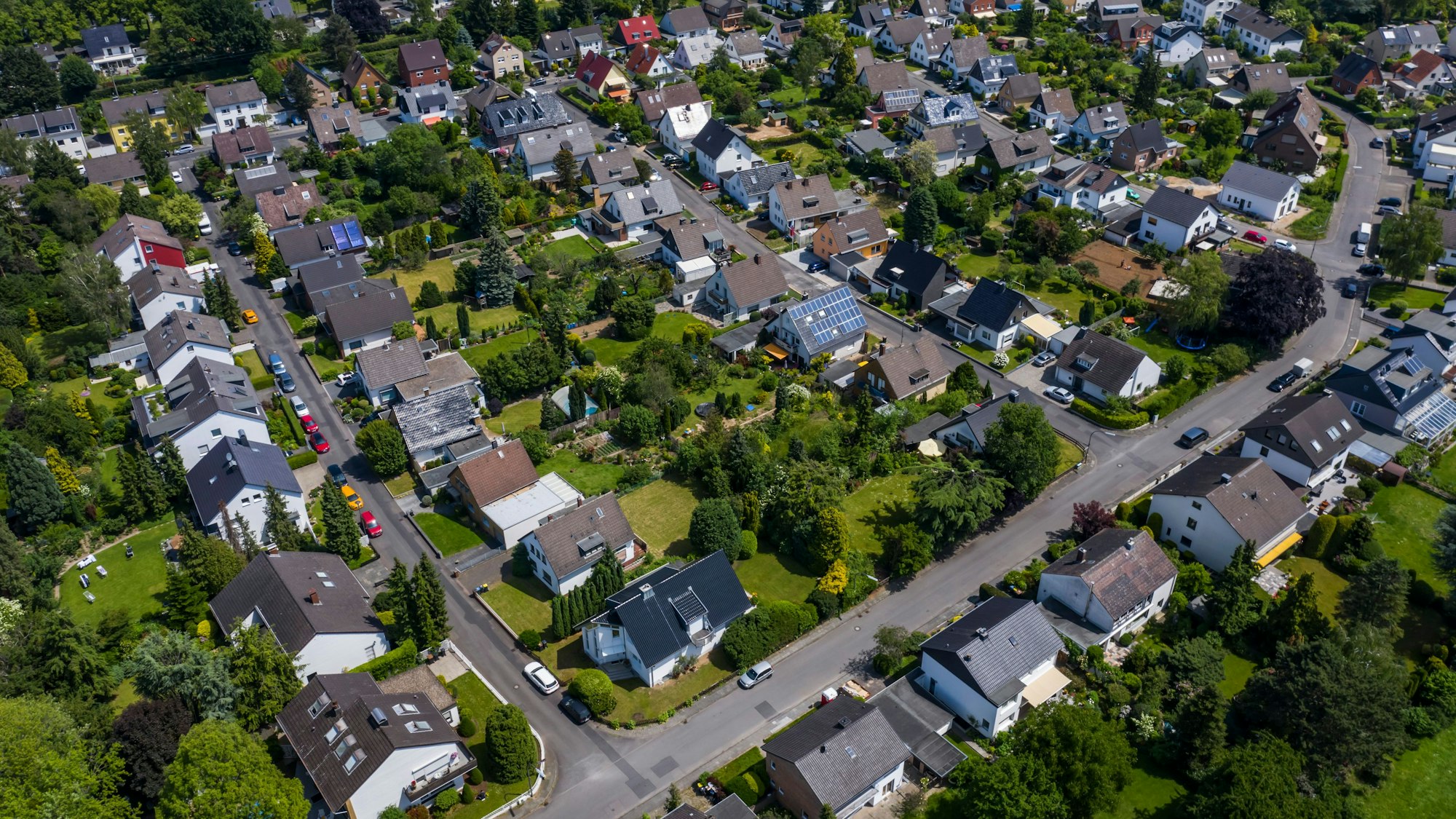 Blick über ein Wohngebiet mit Einfamilienhäusern und mehreren Straßen. In den Gärten stehen zahlreiche Bäume. Das Gebiet hat viele Grünflächen.