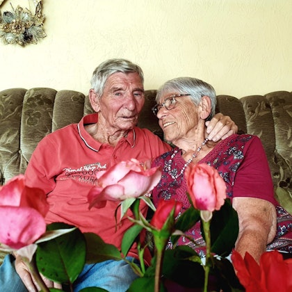 Margret und Bernd Keßenich aus Weilerswist sitzen auf einer Couch und halten sich im Arm. Im Vordergrund sind Rosen.