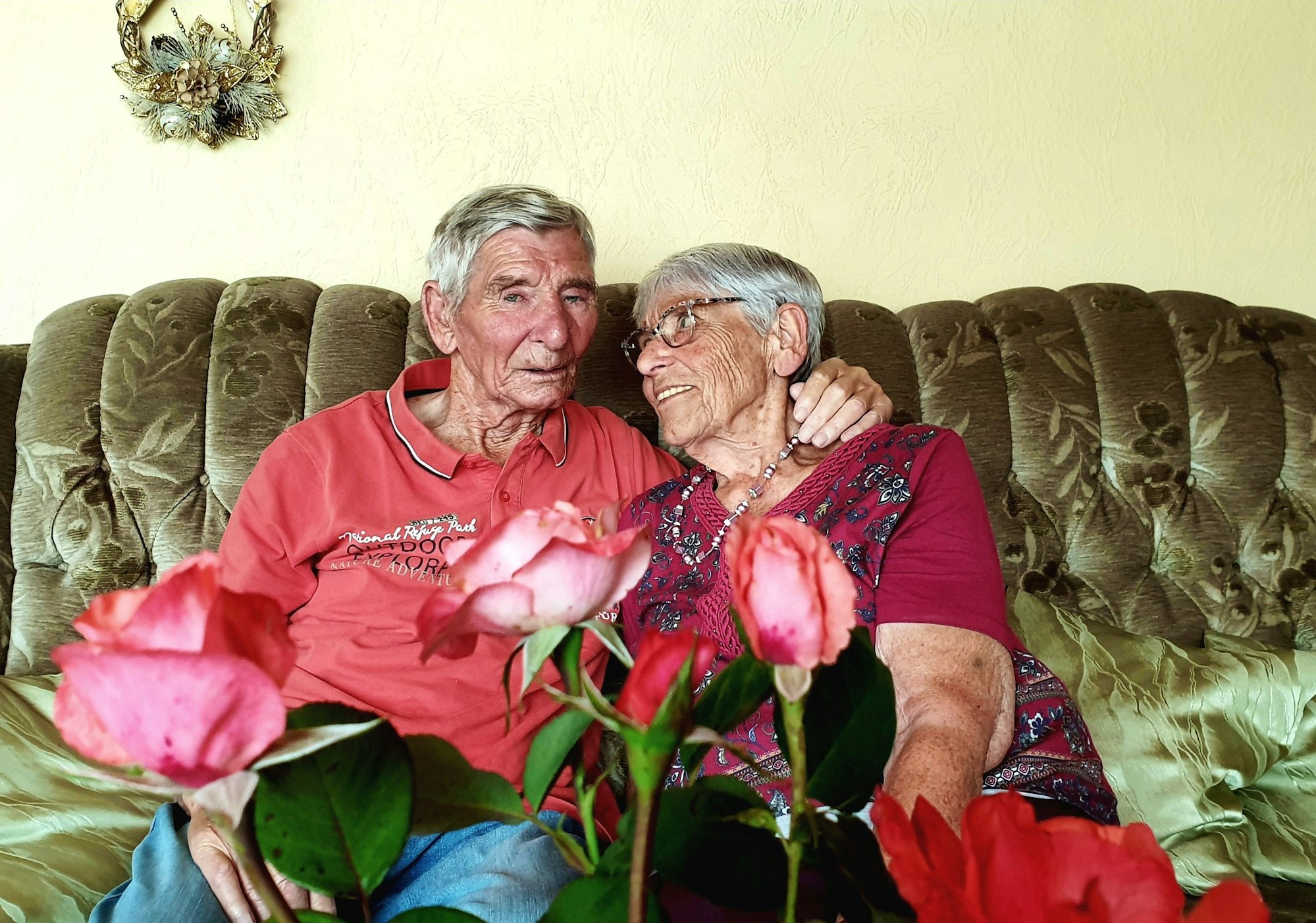 Margret und Bernd Keßenich aus Weilerswist sitzen auf einer Couch und halten sich im Arm. Im Vordergrund sind Rosen.