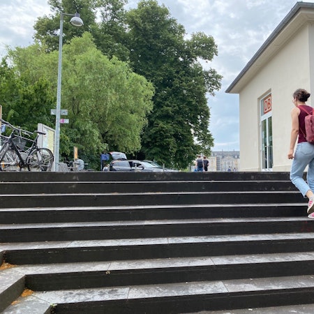 Eine Frau steigt die Treppe zum Bahnhofsvorplatz hinauf. Im Hintergrund ist das Schloss Augustusburg zu sehen.