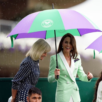 Die britische Prinzessin Kate, Prinzessin von Wales, und die ehemalige Tennisspielerin Debbie Jevans (l) stehen am Dienstag, 4. Juli 2023, während des Erstrundenmatches im Dameneinzel unter Regenschirmen.