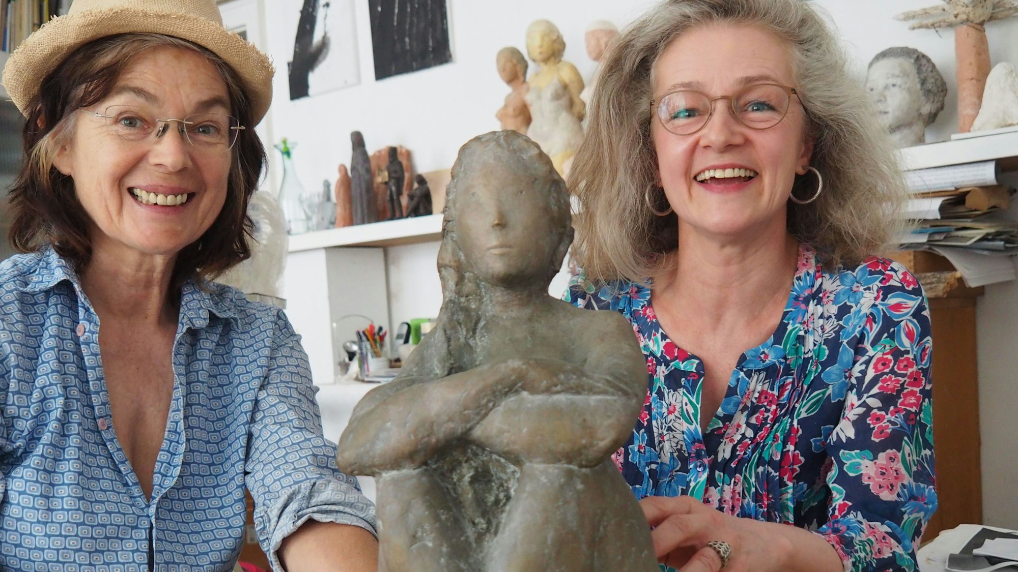 Die beiden Künstlerinnen lächeln in die Kamera – in ihrer Mitte sitzt die Plastik.