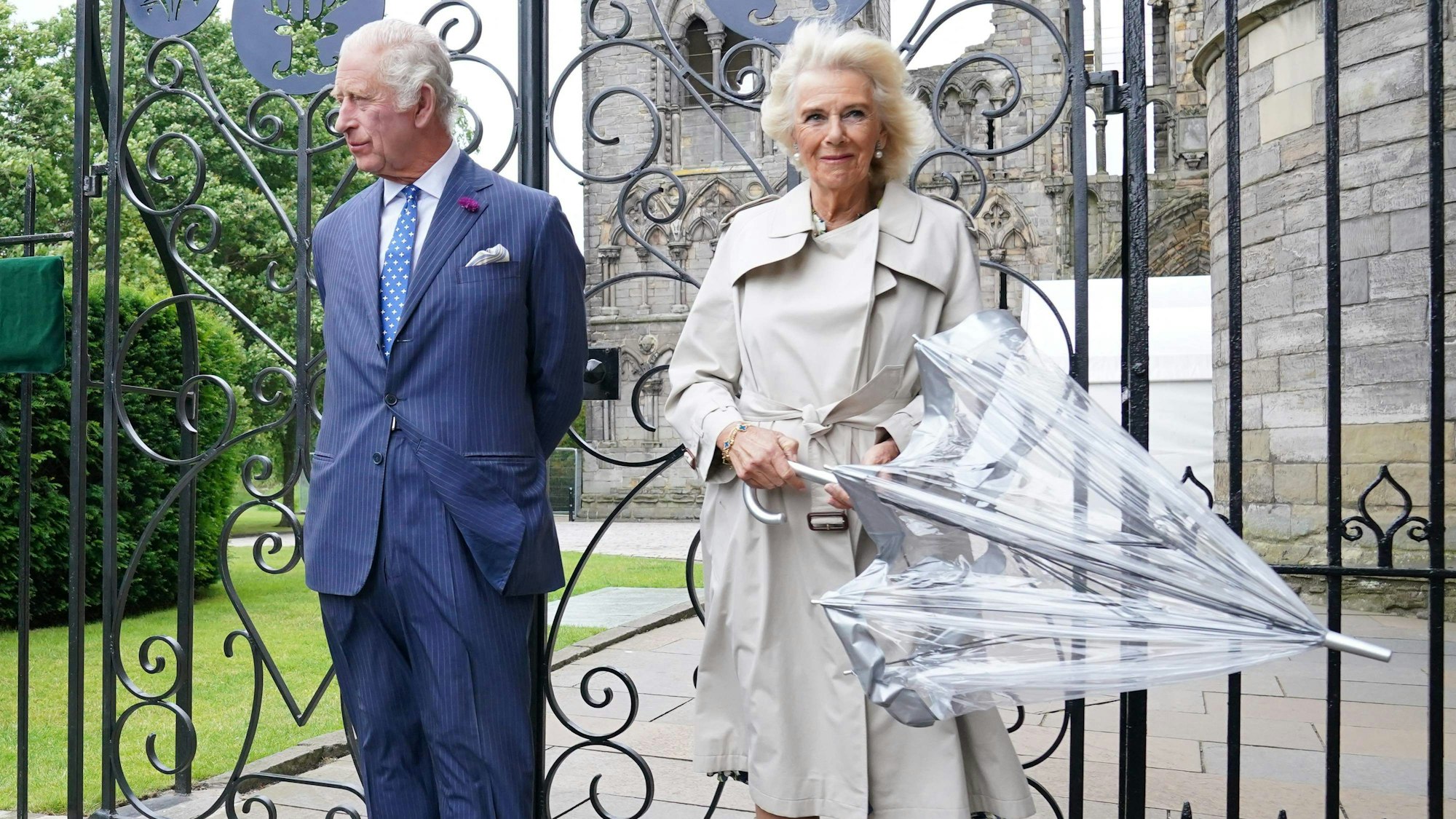 Königin Camilla (r) neben König Charles vor einem Tor.