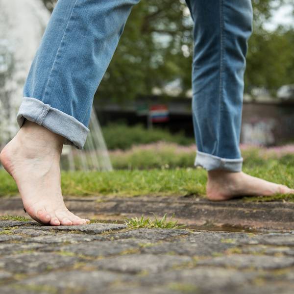 Eine Person geht barfuß in einem Park von einem Gehweg auf eine Wiese